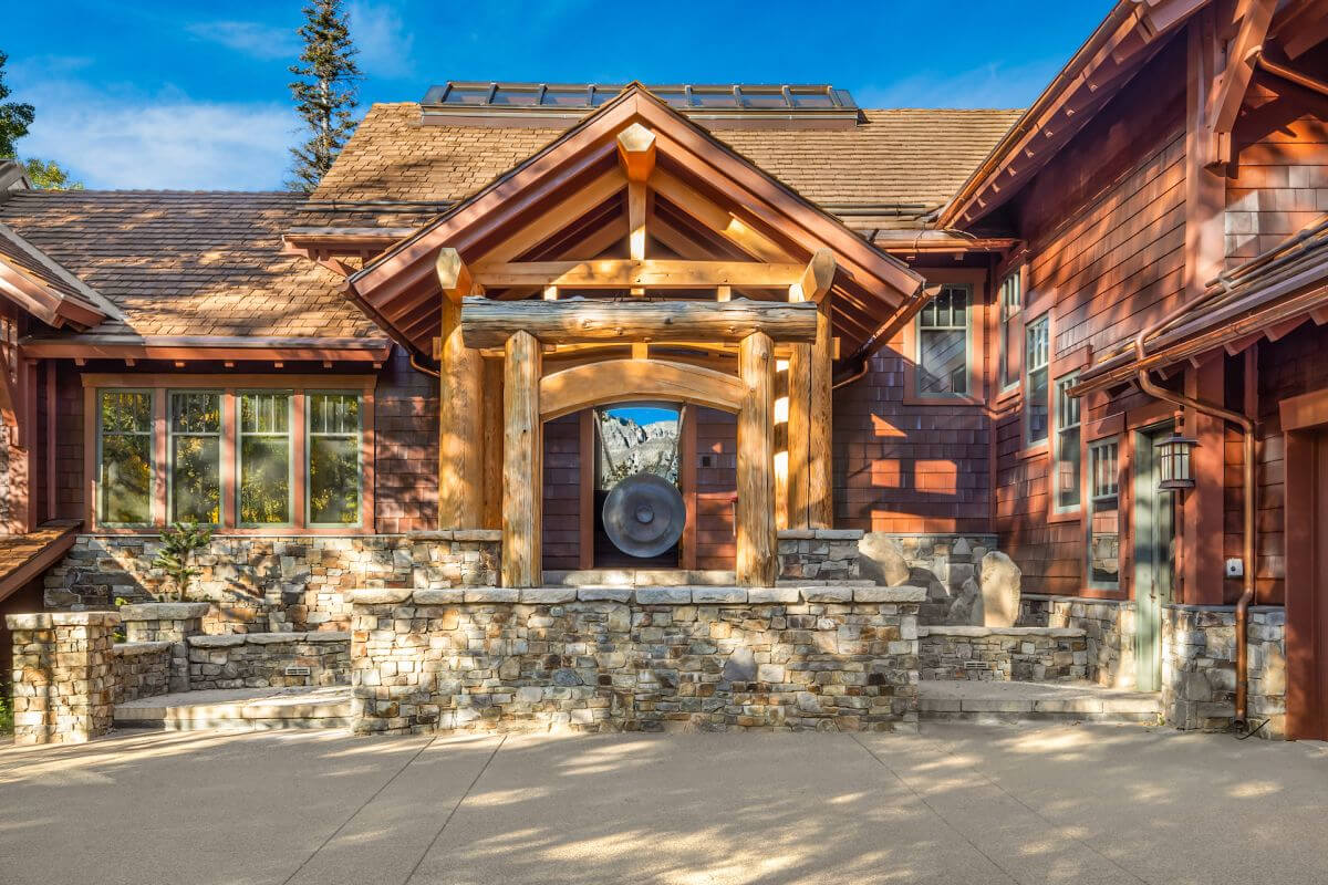Rustic lodge exterior with stone steps and a wooden arched entryway, a large gong visible inside the arch.